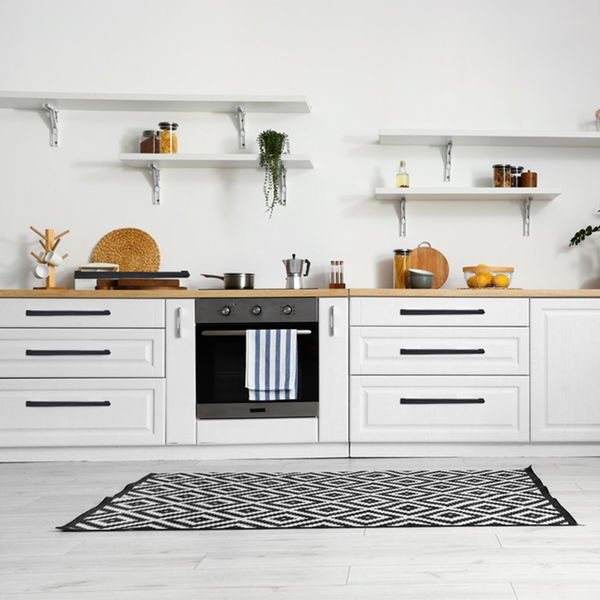 Modern kitchen with white cabinets, wooden countertops, and open shelves holding jars, plants, and kitchenware. An oven with a striped towel is centered below the shelves, and a patterned rug is on the floor.