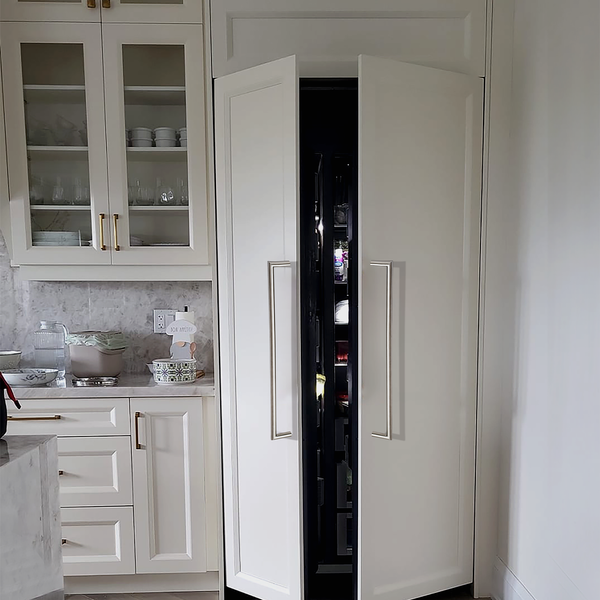 A modern kitchen with cream-colored cabinets and gold handles. One tall cabinet door is open, revealing a refrigerator hidden behind matching cabinet panels for a seamless look.
