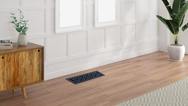 A modern room with white paneled walls, wooden flooring, a mid-century wooden console, a potted plant, a floor vent, and part of a patterned rug. Two tall windows let in natural light.