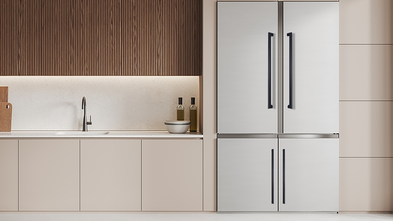 Modern kitchen with light beige cabinets, a sink, and two bottles and a bowl on the countertop. A large stainless steel, four-door refrigerator stands to the right. Vertical wood paneling decorates the backsplash.