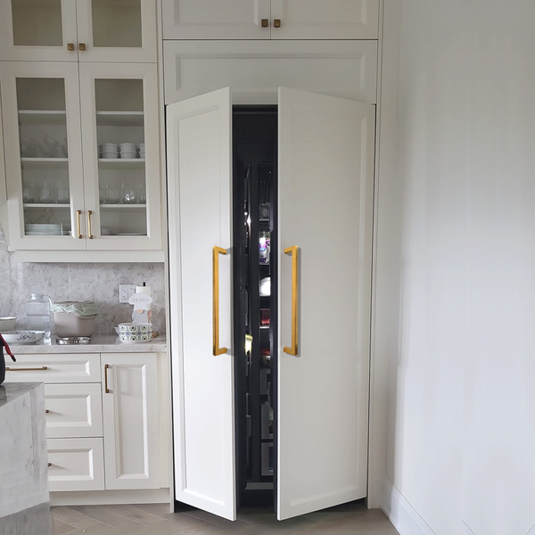 A modern kitchen with white cabinets and gold handles, featuring a refrigerator hidden behind matching cabinet doors that are partially open.