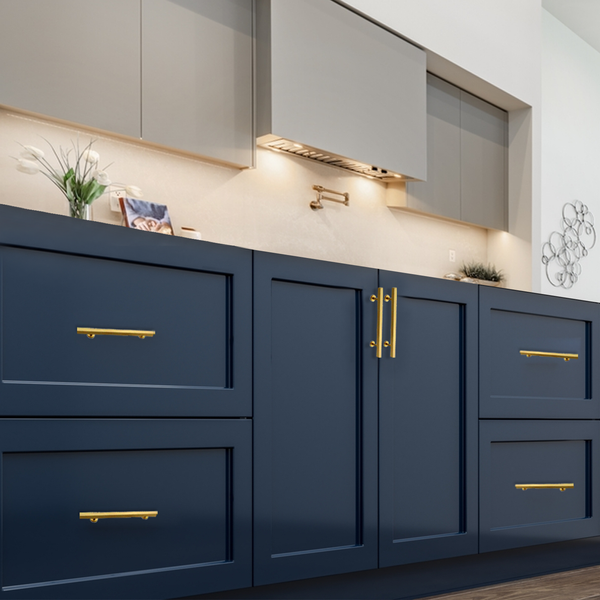 Modern kitchen with navy blue lower cabinets featuring gold handles, light beige upper cabinets, under-cabinet lighting, and light-colored countertops. Decorative items and a wall art piece are visible.