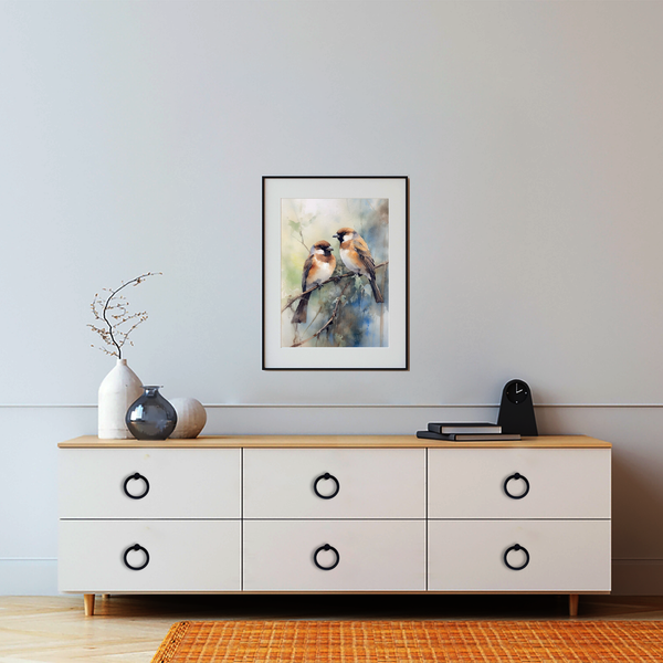A modern dresser with black circular handles sits against a light gray wall. On top are a white vase with twigs and a black clock. Above hangs a framed painting of two birds perched on a branch.