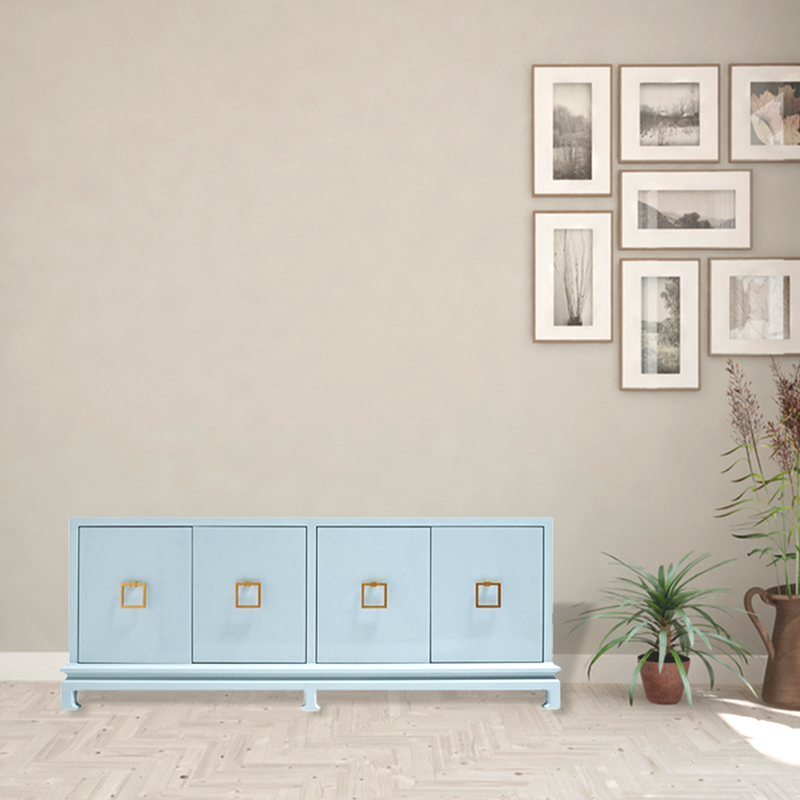 A minimalist living room with a light blue cabinet, plants on the floor, and a beige wall decorated with a grid of framed nature photographs.