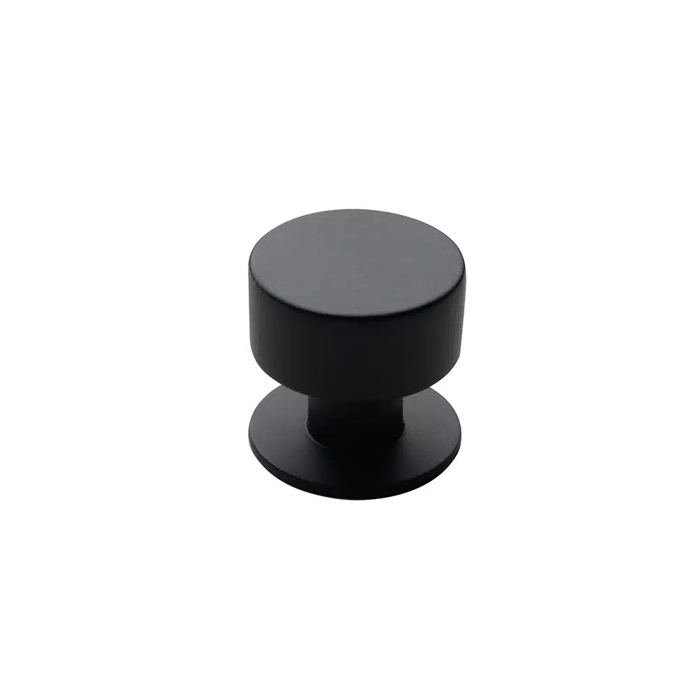 A black, cylindrical cabinet knob by Taymor Industries, crafted from durable Zinc Die-Cast with a flat top and round base, is shown against a plain white background.