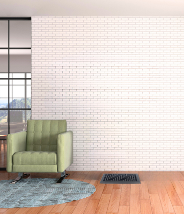 A green armchair sits on a round blue rug atop a wooden floor, next to a wall vent, in front of a white brick wall with glass windows to the side.