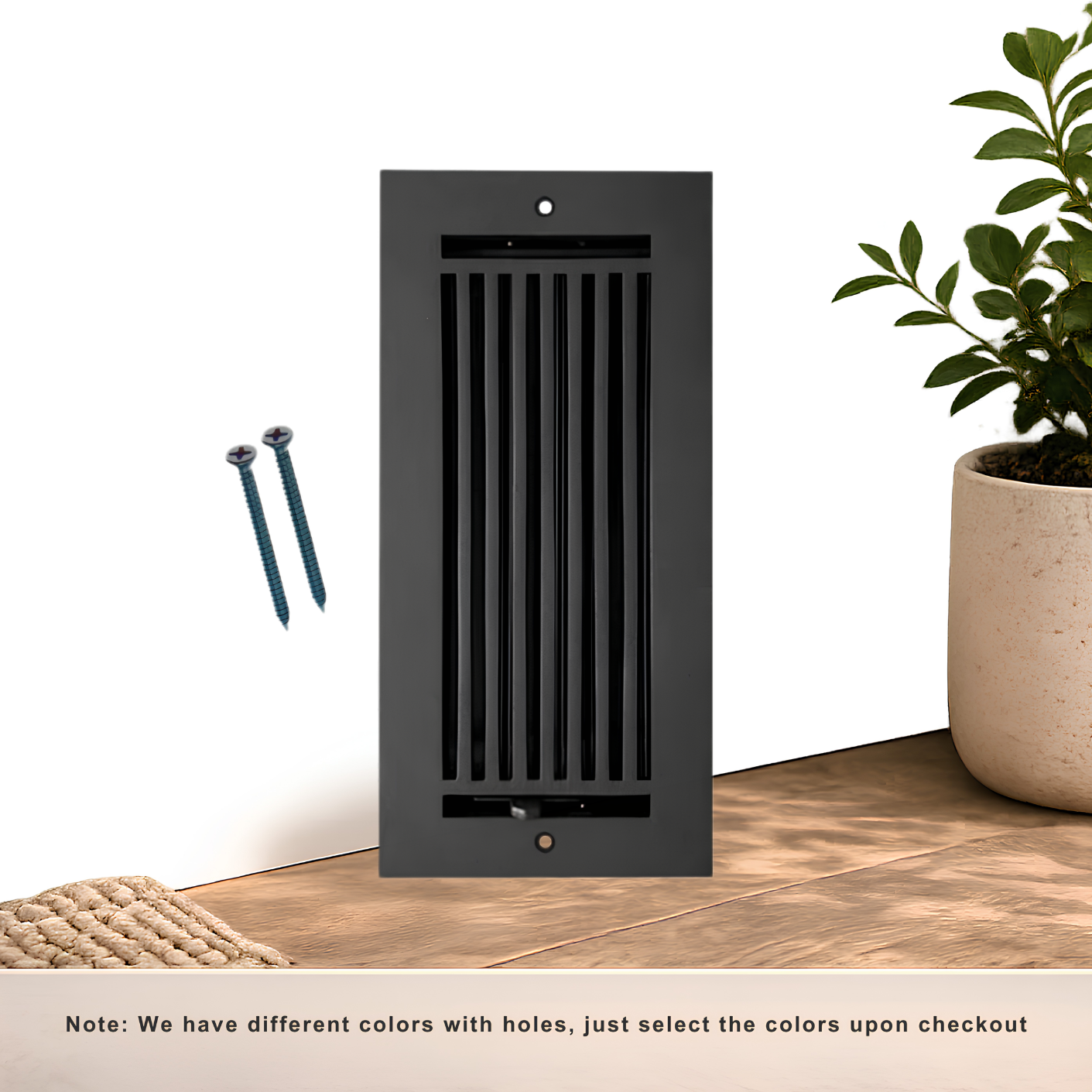 Black decorative wall vent on a wooden floor with a plant and screws nearby.