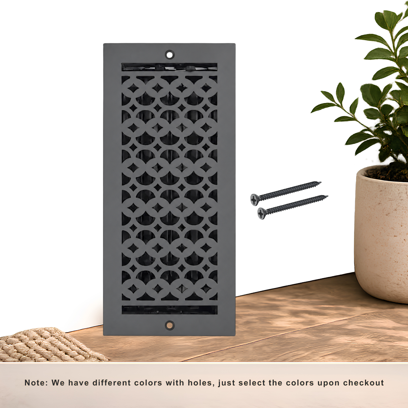 A dark gray decorative wall vent with a geometric cutout pattern, shown standing on a wooden surface.