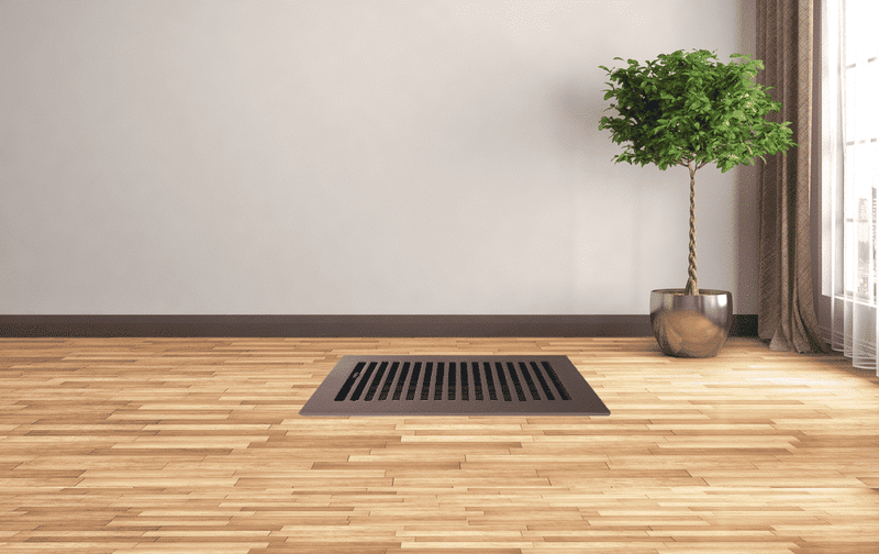 Floor vent on a wooden floor with a plant in the background