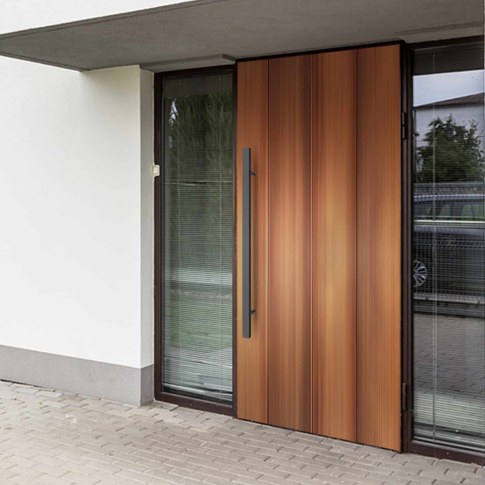 Prima Decorative Hardware modern wooden front door with vertical panels and a sleek black matte handle, framed by large glass side panels with blinds, on a light-colored building with a paved entryway.