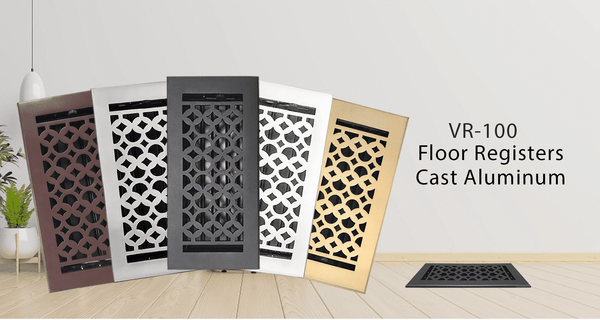 Five decorative floor registers in black, silver, and gold finishes are displayed upright in a modern room with a plant and lamp. Text reads: VR-100 Floor Registers Cast Aluminum.