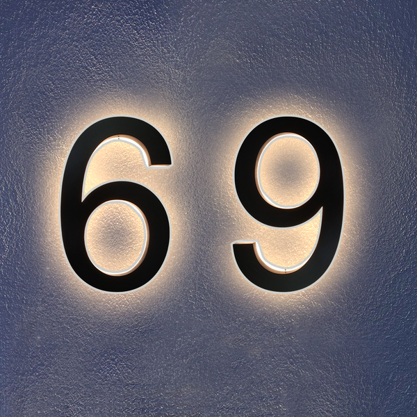 Black numbers 6 and 9 are mounted on a textured gray wall, each outlined by a glowing white backlight that creates a halo effect around the numbers.