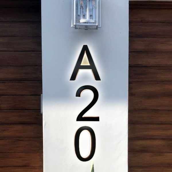 Large black letters and numbers A20 are mounted vertically on a white pillar, illuminated by a wall light above; the background features brown wooden paneling.