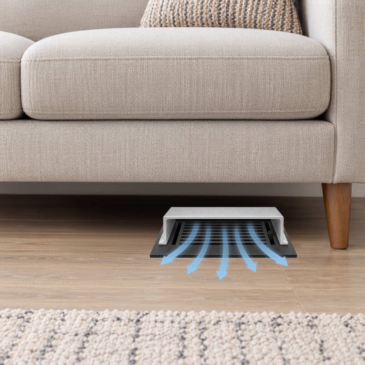 A silver deflector installed under a beige sofa on a wood floor.
