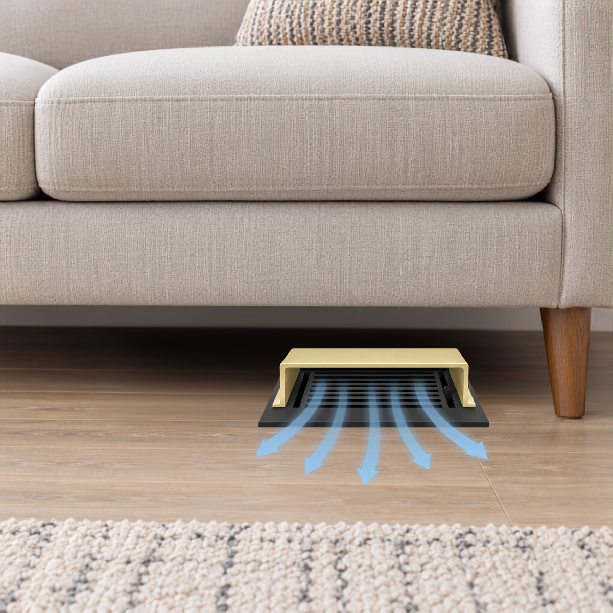 A gold deflector installed under a beige sofa on a wood floor.
