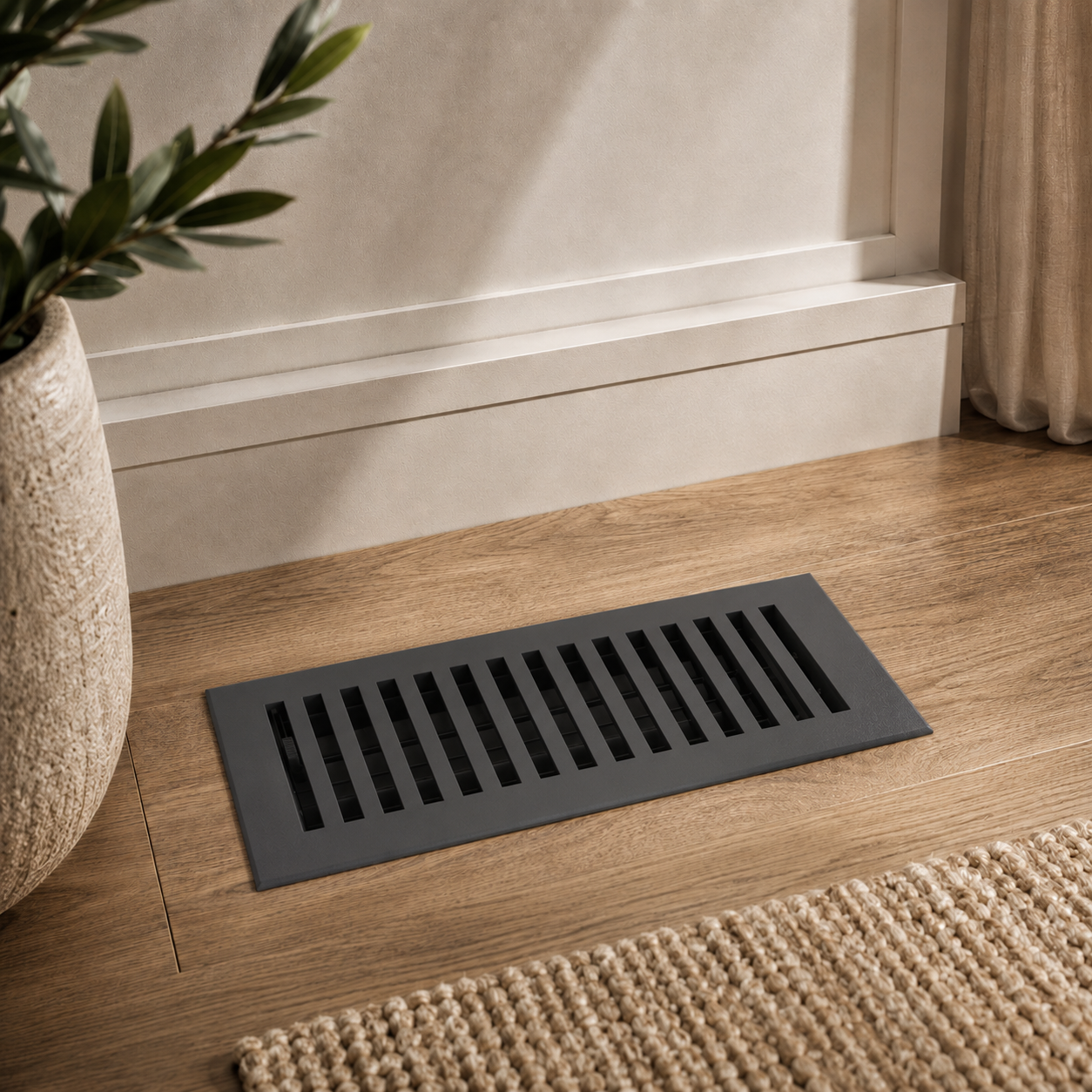 Decorative black floor vent on a wooden floor with a plant and rug in the background
