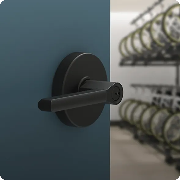 A black door handle on a blue door, slightly open, revealing a room with several bicycles stored on racks in the background.
