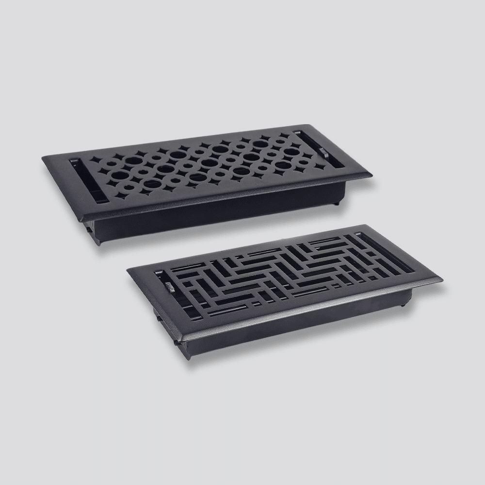 Two black metal floor vent covers with decorative geometric cutout patterns, one with a circular motif and the other with a rectangular maze-like design, placed on a light gray background.