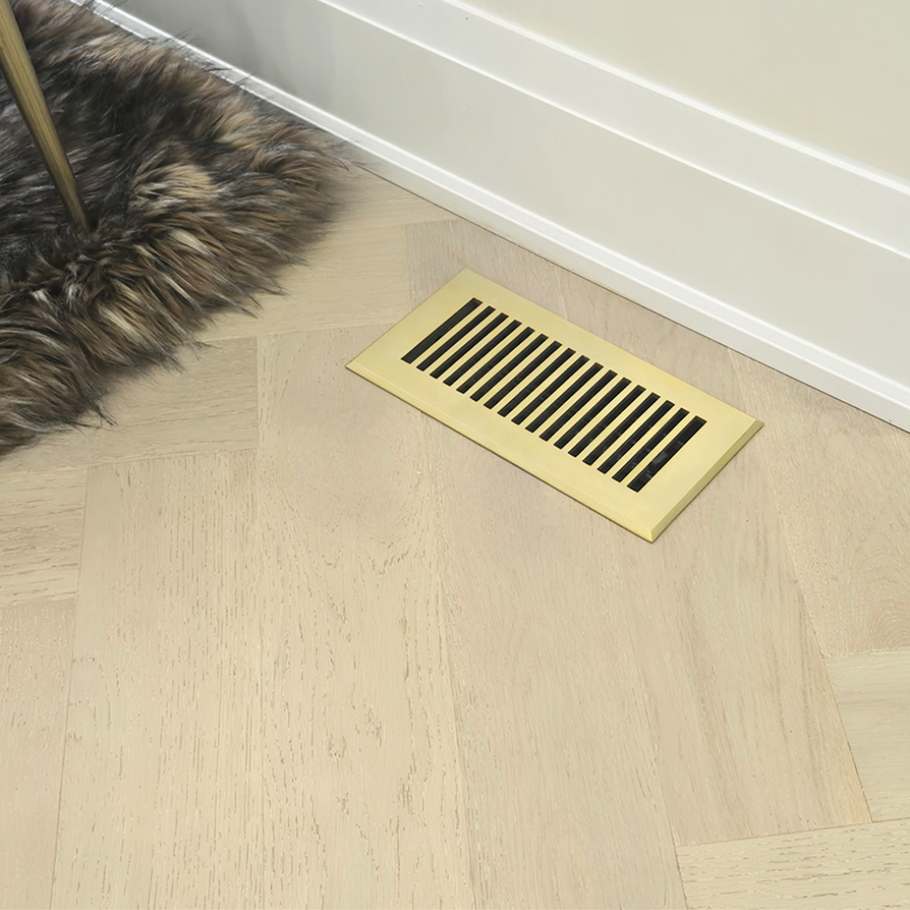Gold floor vent on a wooden floor with a fur rug partially visible.